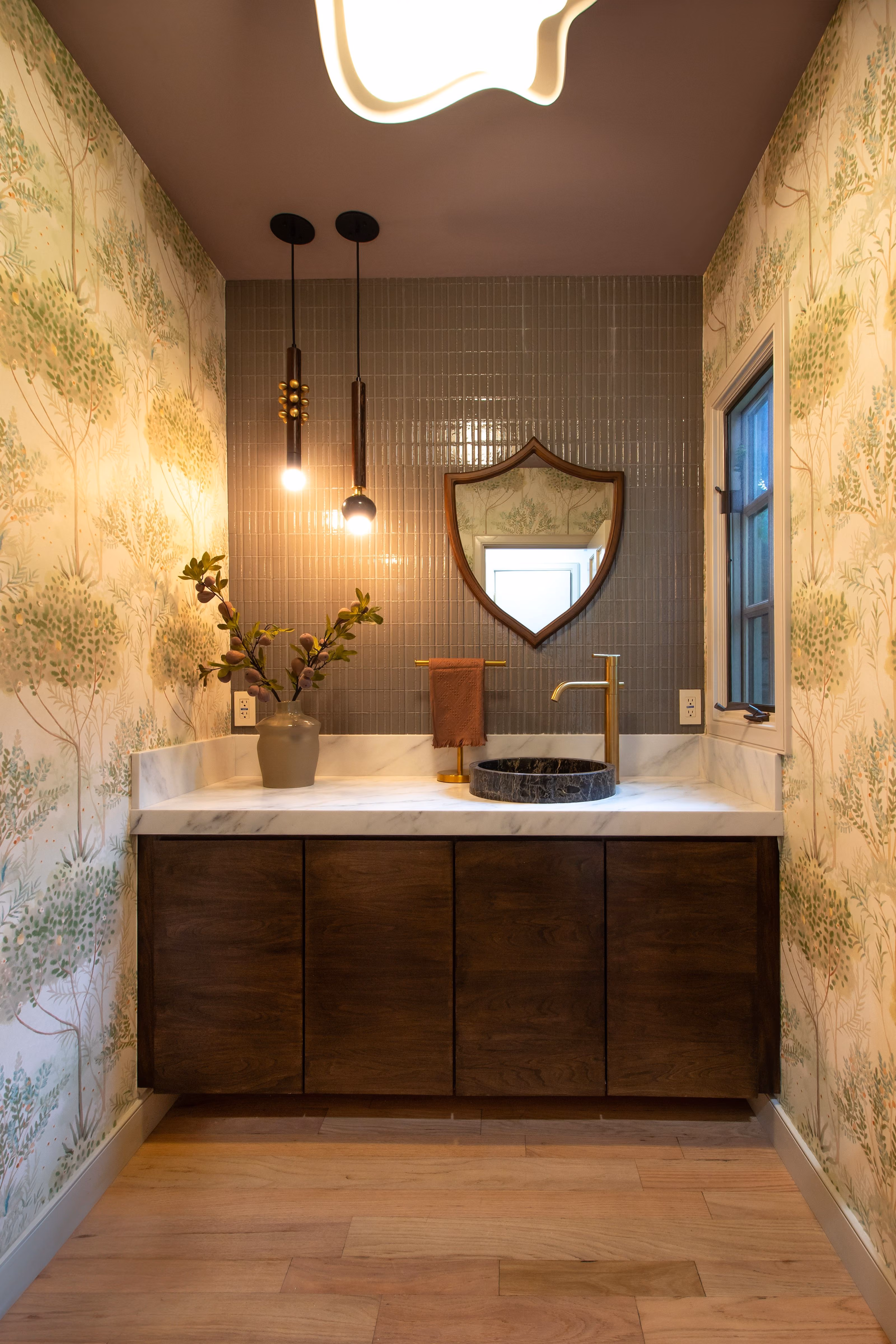 Modern bathroom vanity with marble countertop, black circular sink, decorative mirror, and wallpapered walls.