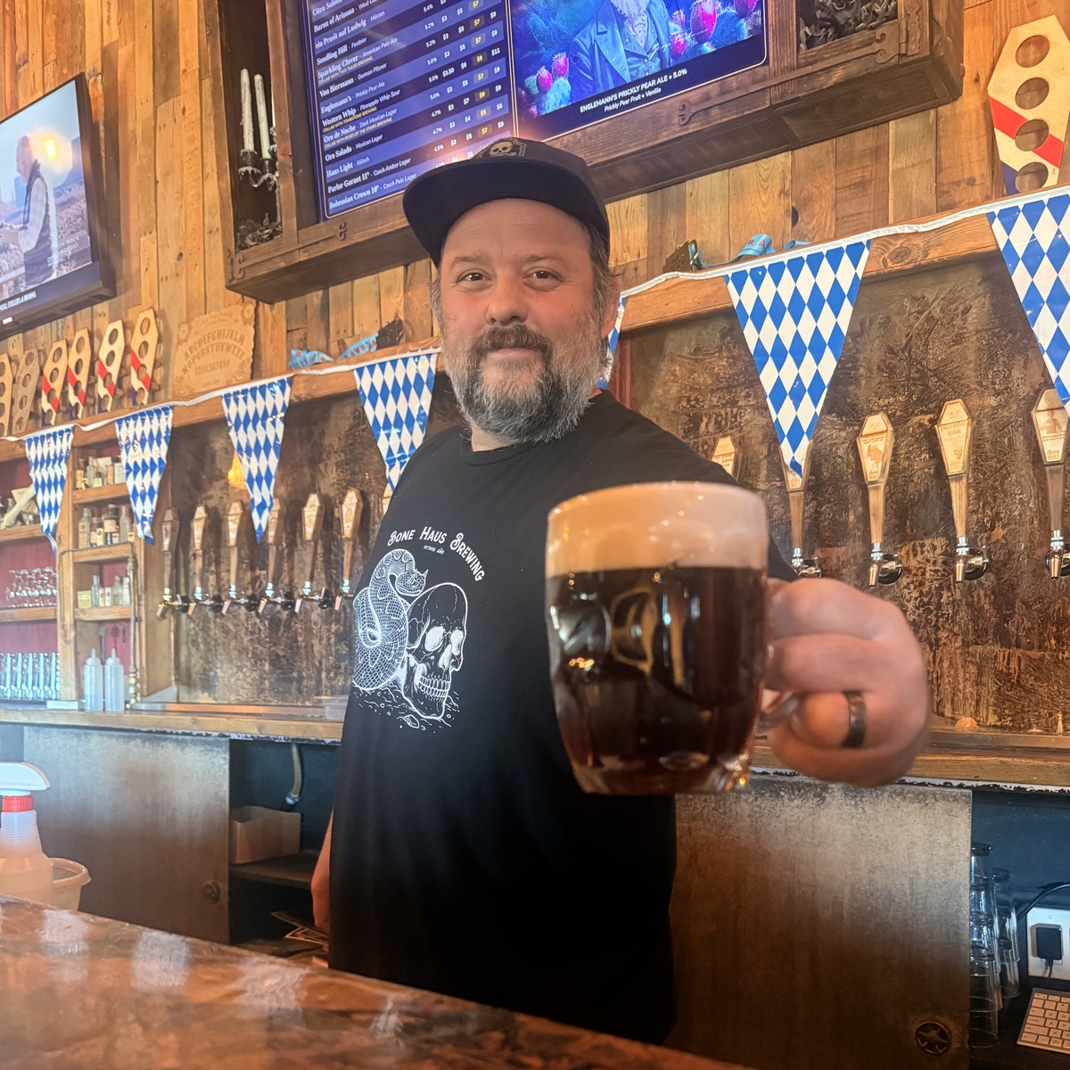 DJ Mannila, Bone Haus Tap Room Manager, holding a beer behind the taproom bar