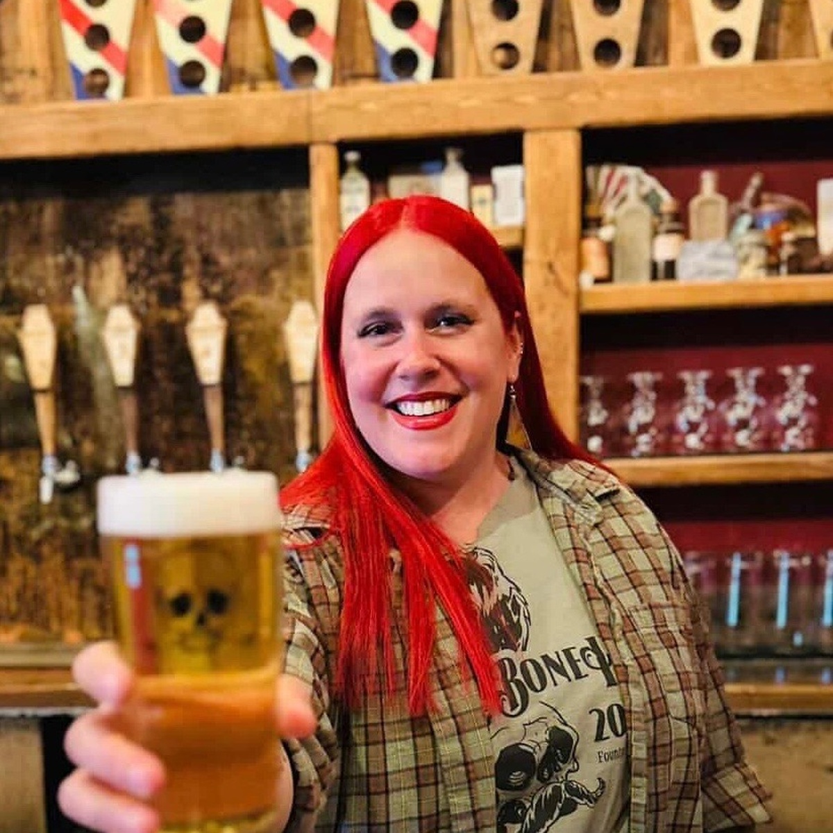 Rachel Benkowski smiling and offering a beer behind the Bone Haus taproom bar