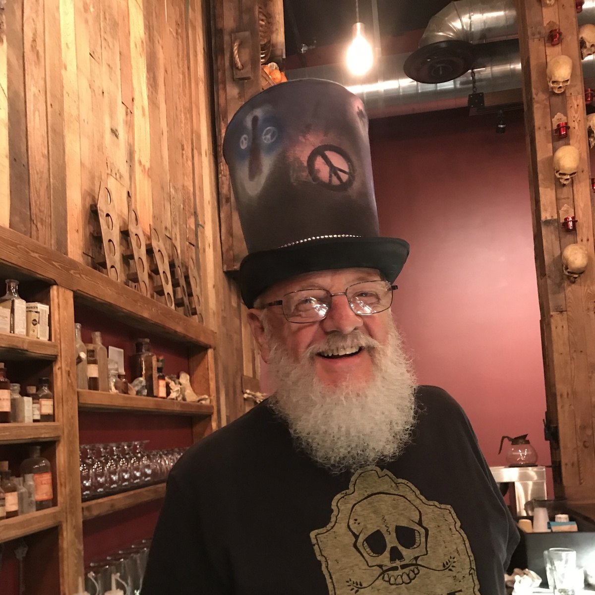 Sam Chapman smiling behind the Bone Haus bar in a tall decorated hat and Bone Haus shirt