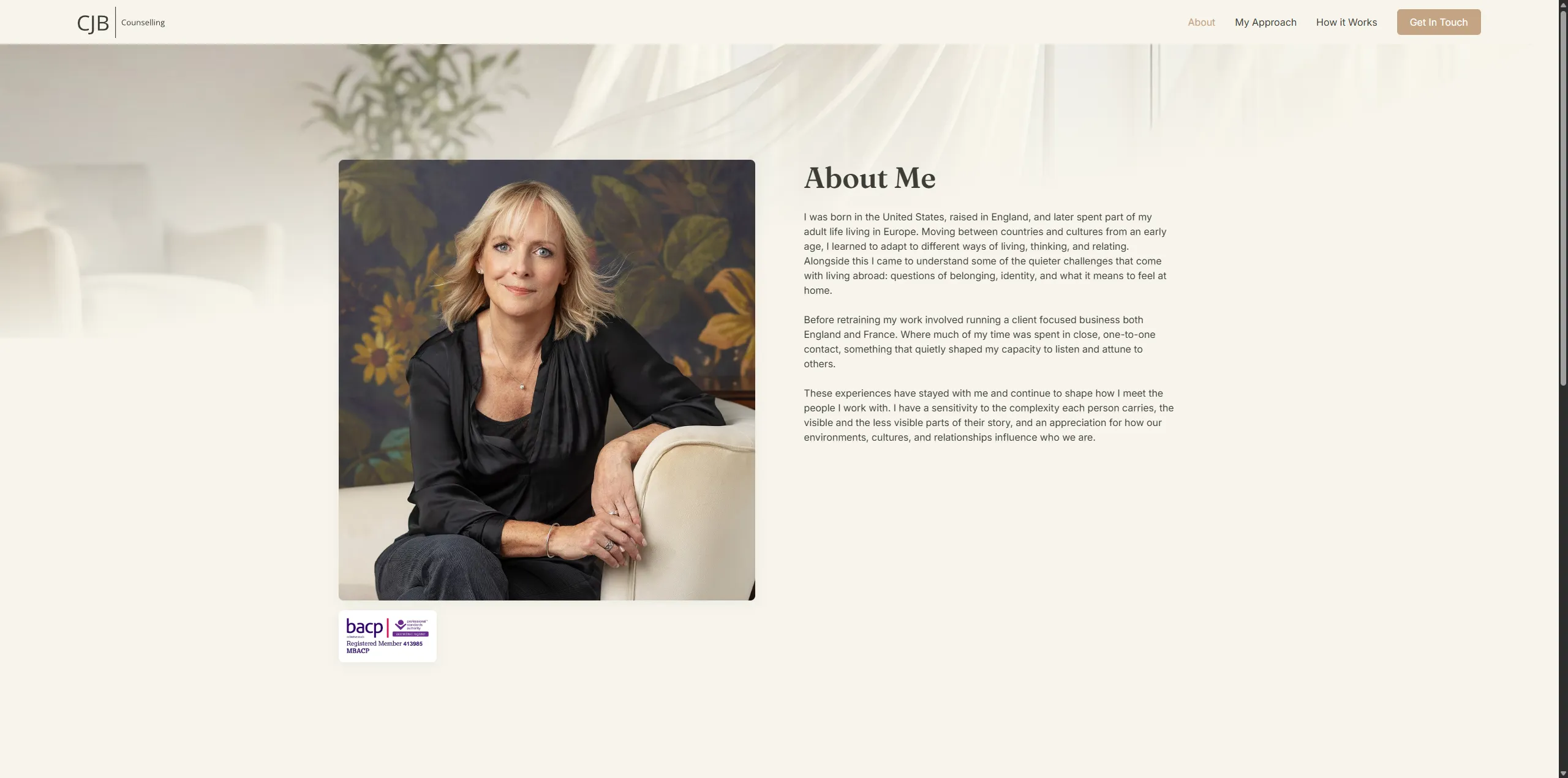 Woman with blonde hair in black shirt sitting on a white chair against floral backdrop.