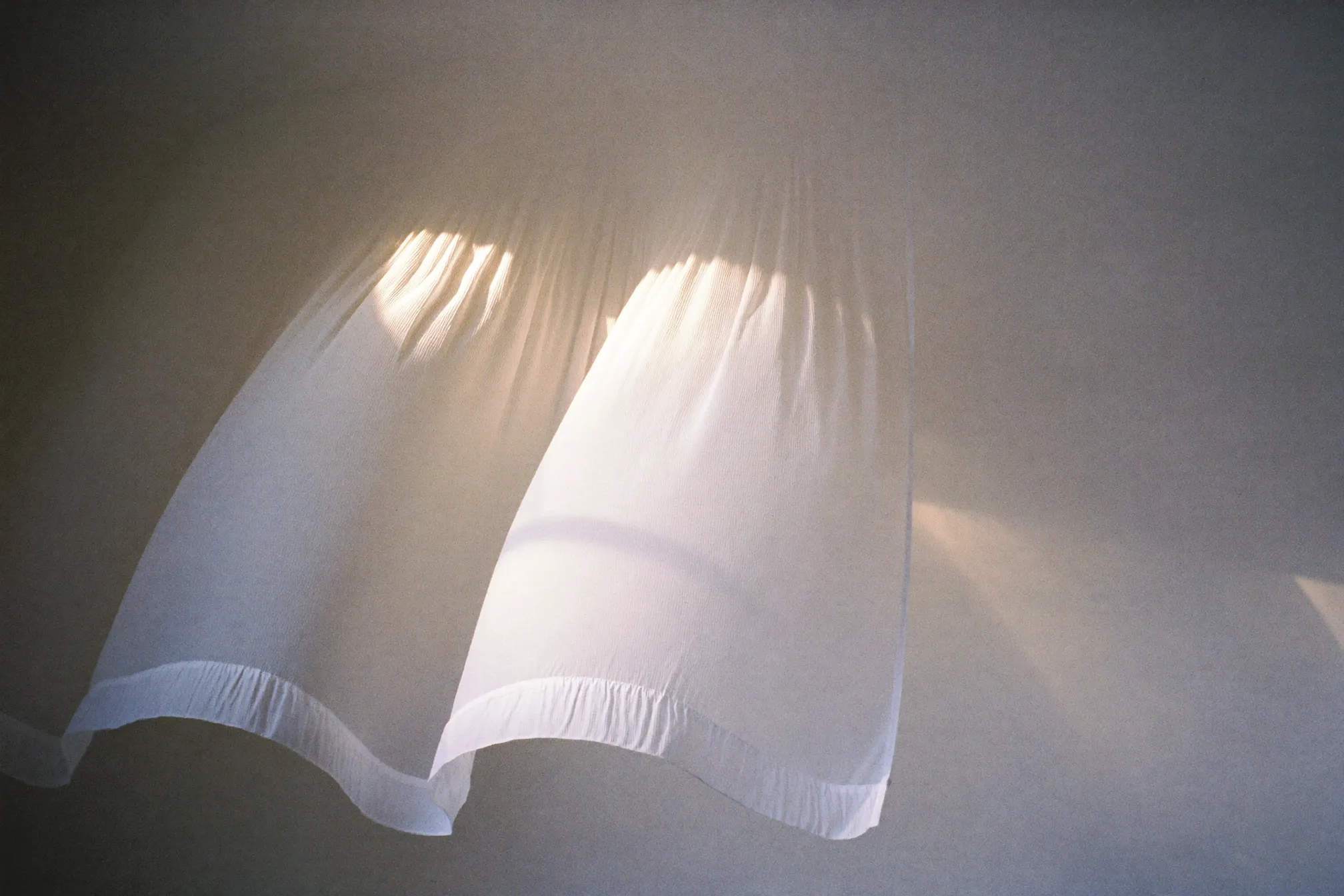 Sheer curtain drifting in soft sunlight, calm and clean
