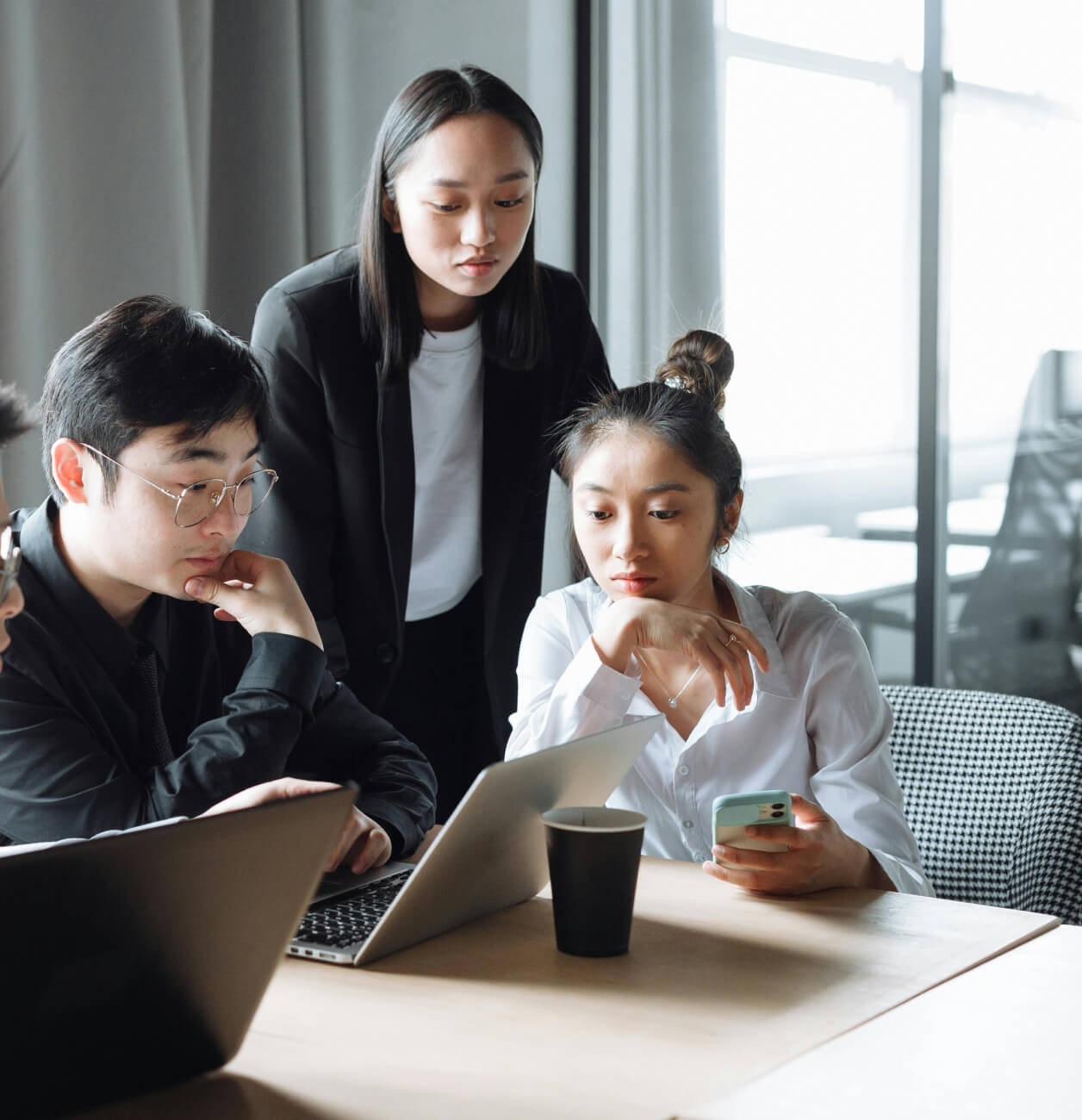 Drei junge asiatische Berufstätige arbeiten gemeinsam an Laptops in einem modernen Büro.