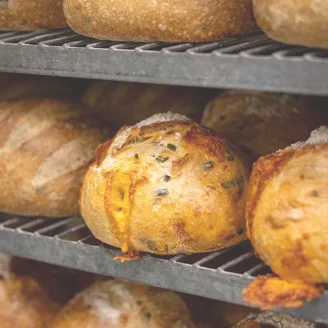 Golden crusty cheese bread with herbs cooling on a rack alongside other loaves.