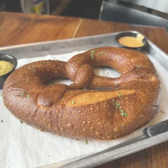 Large soft pretzel with coarse salt on a tray with mustard and cheese dipping sauces.