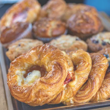 Tray of assorted golden brown pastries, including danishes and muffins, fresh and flaky.
