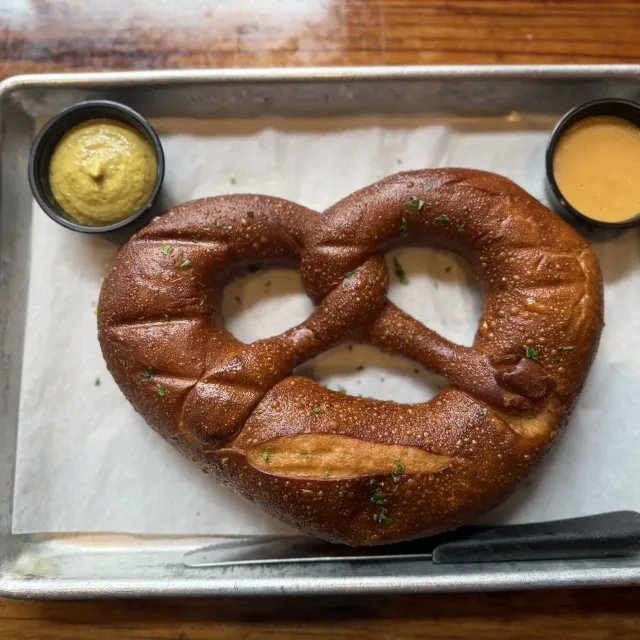 Large soft pretzel on tray with mustard and cheese dipping sauces on each side.