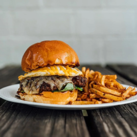 Cheeseburger with lettuce and fries on a white plate over a wooden table.