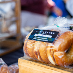 Packaged loaf of bread labeled 'Cake & Bacon' displayed on a wooden surface at a market stall.