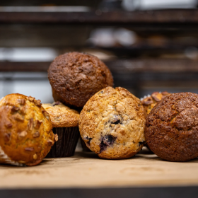 Assorted muffins including chocolate and blueberry on a wooden surface with a blurred background.