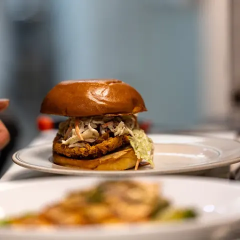 Close-up of a fried chicken sandwich with coleslaw in a soft bun on a white plate.