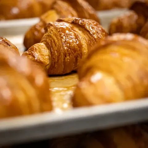 Golden-brown croissants with flaky layers on a baking sheet.