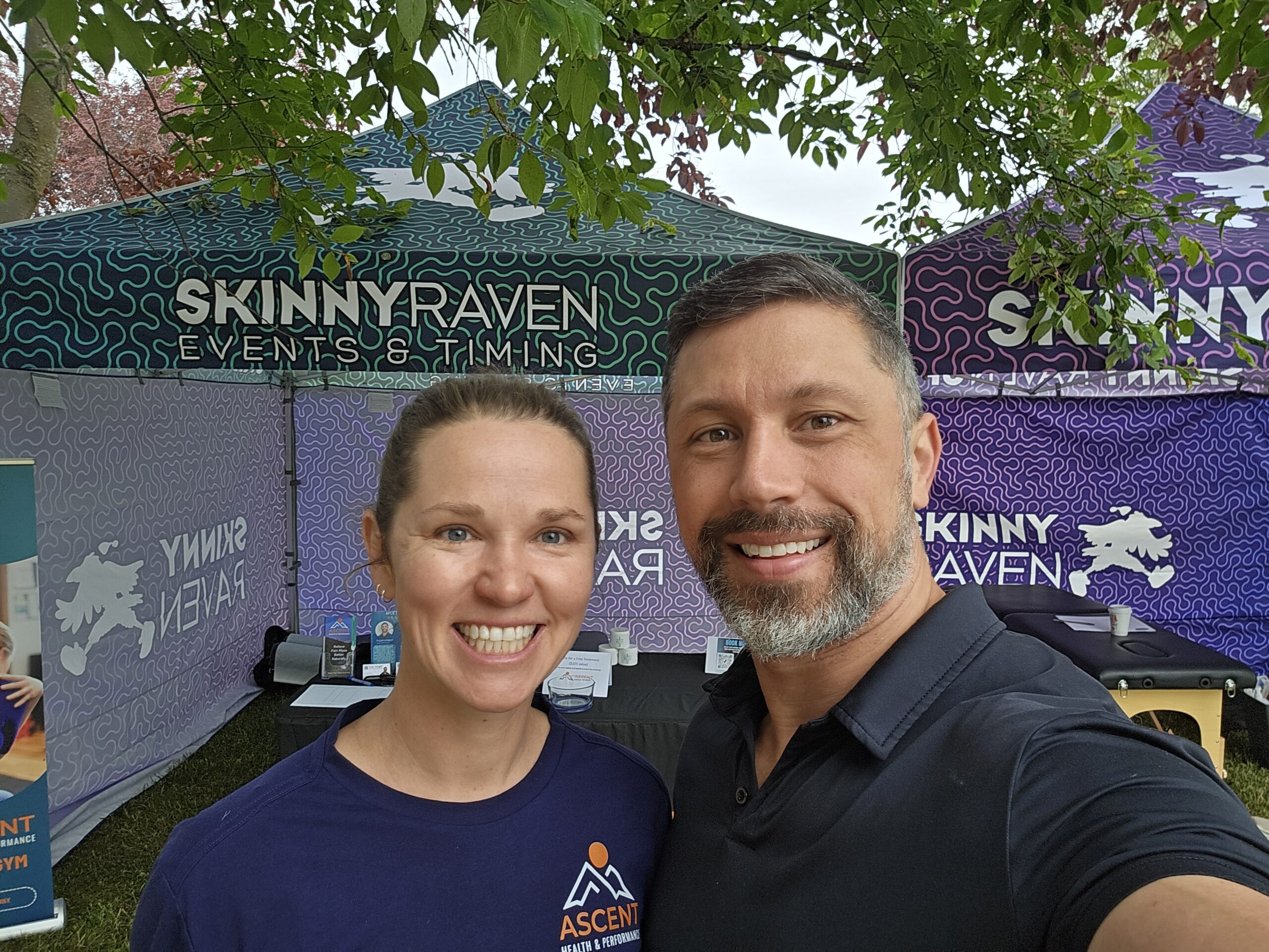 Smiling man and woman taking a selfie outside a tent with Skinny Raven Events & Timing branding.