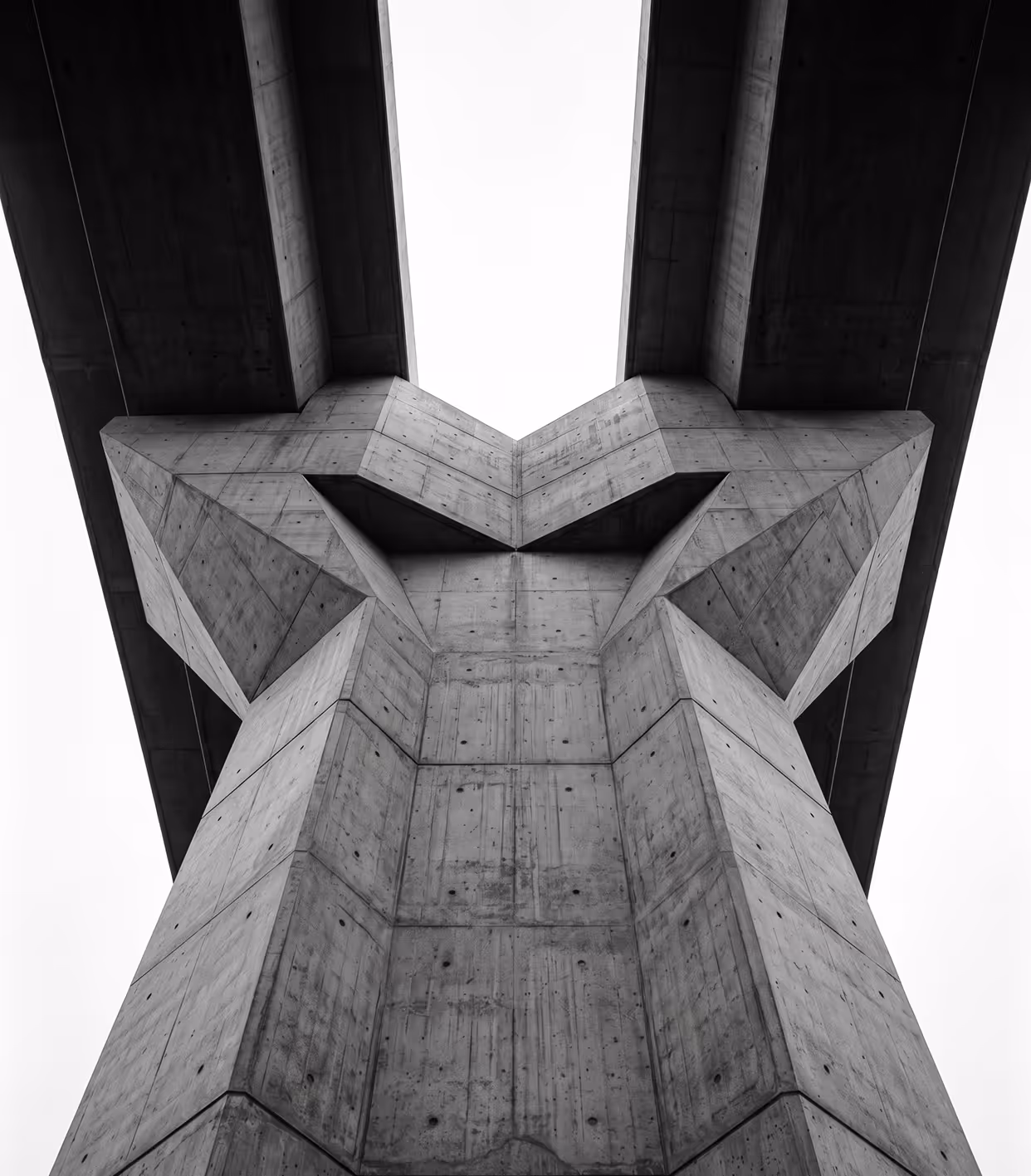 Upward view of a large concrete bridge support with sharp geometric angles in black and white.