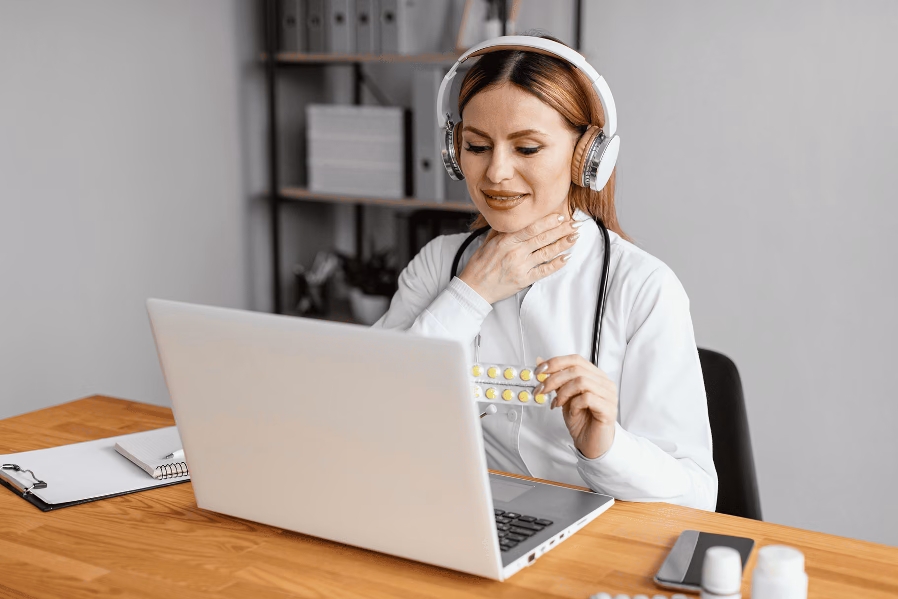 Female doctor with headset holding yellow pills and touching her throat during a video call.