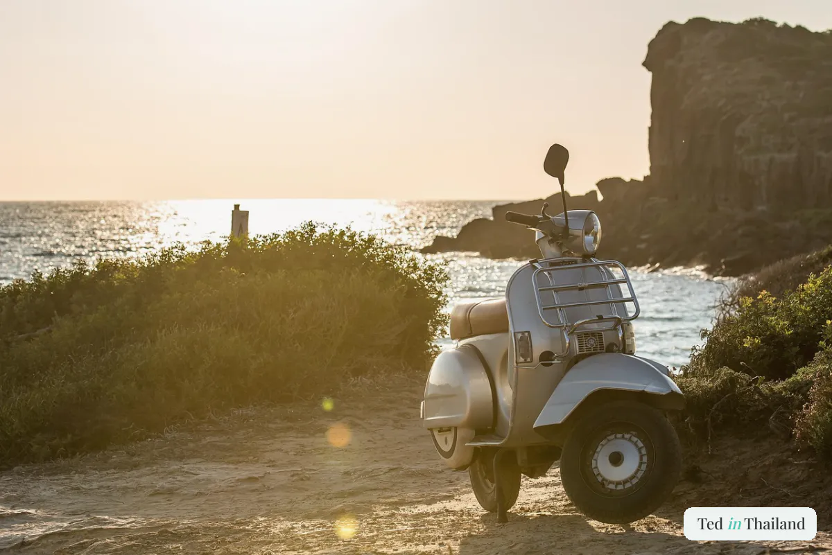 A classic silver scooter parked on a coastal dirt track at golden hour beside the sea on Koh Samui