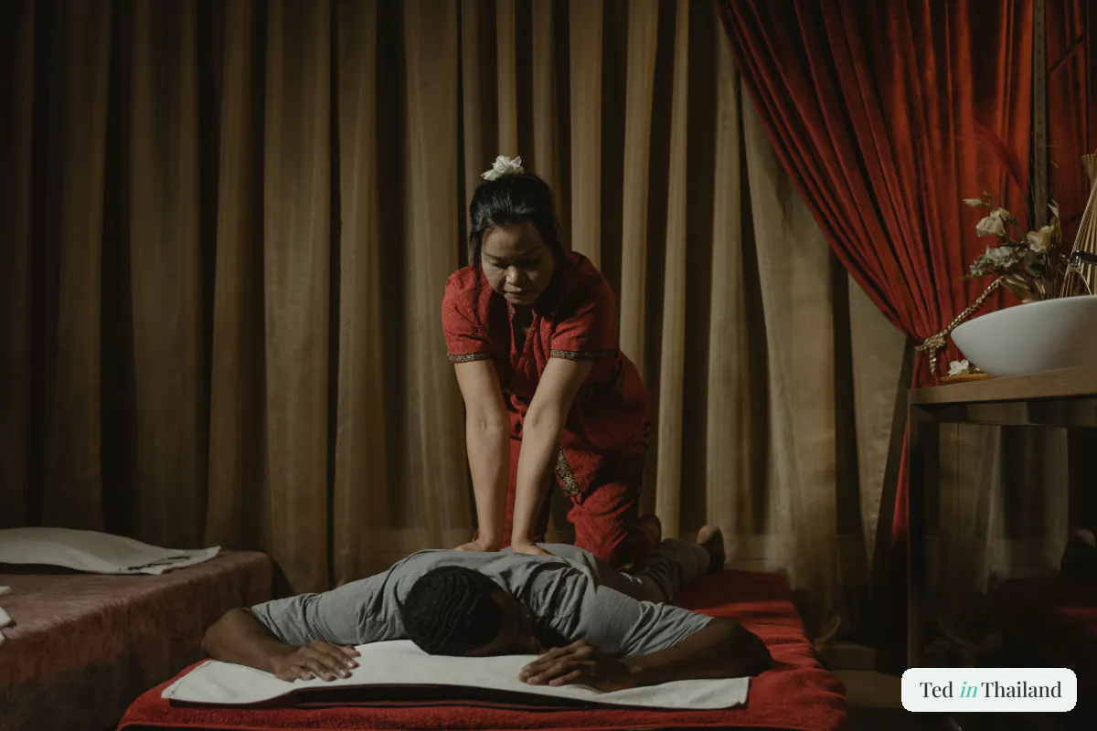 A therapist in a red traditional dress giving a Thai massage to a client on a mat at a Koh Samui spa