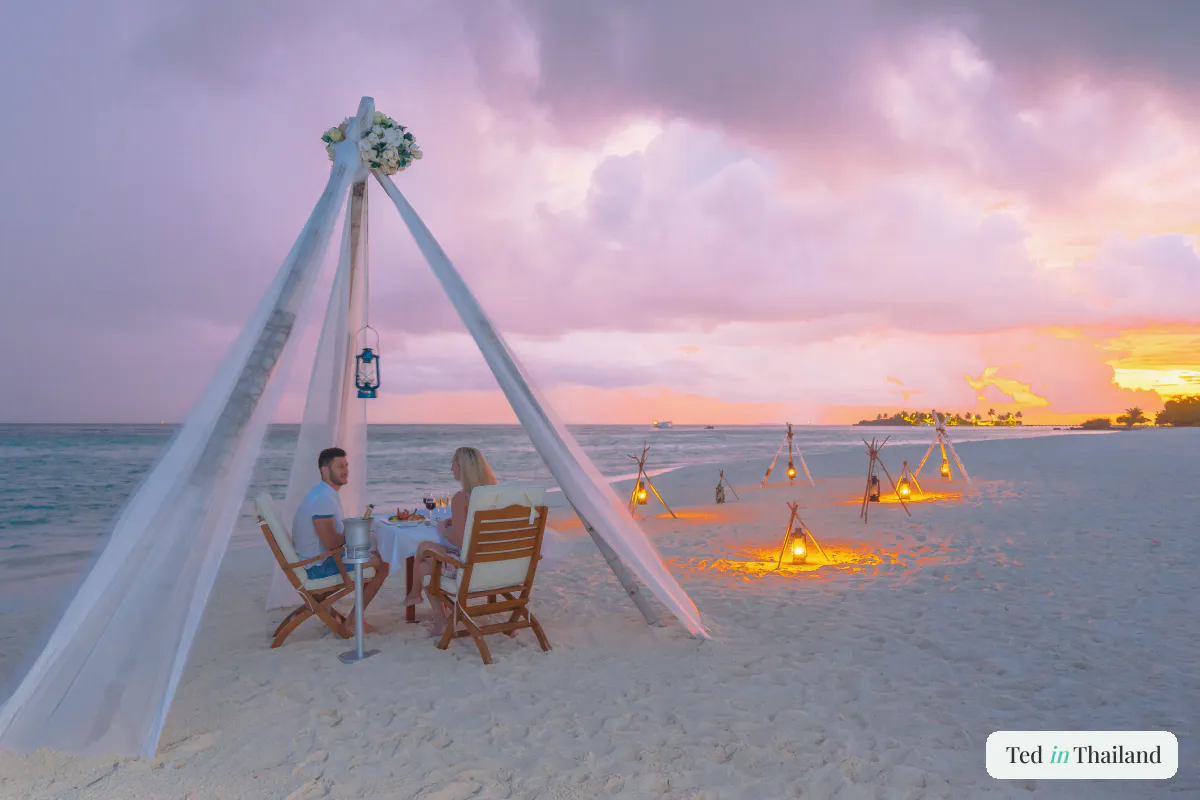 A couple sharing a private candlelit dinner under white drapes on a Koh Samui beach at sunset