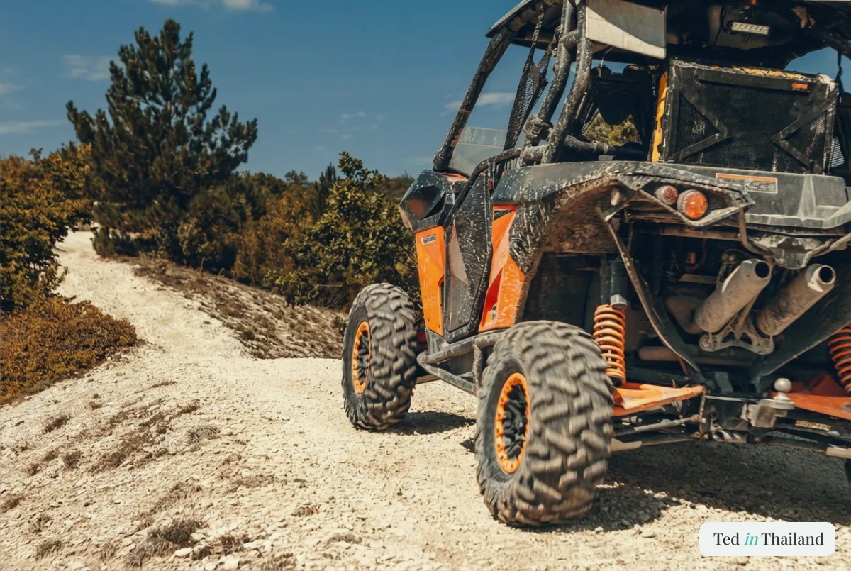 An orange off-road buggy splashed with mud on a rugged gravel trail during an ATV adventure in the hills of Koh Samui