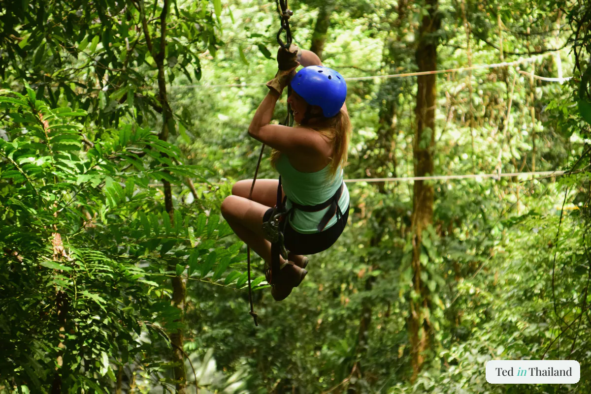 A woman in a harness and helmet ziplining through the dense tropical rainforest canopy on Koh Samui