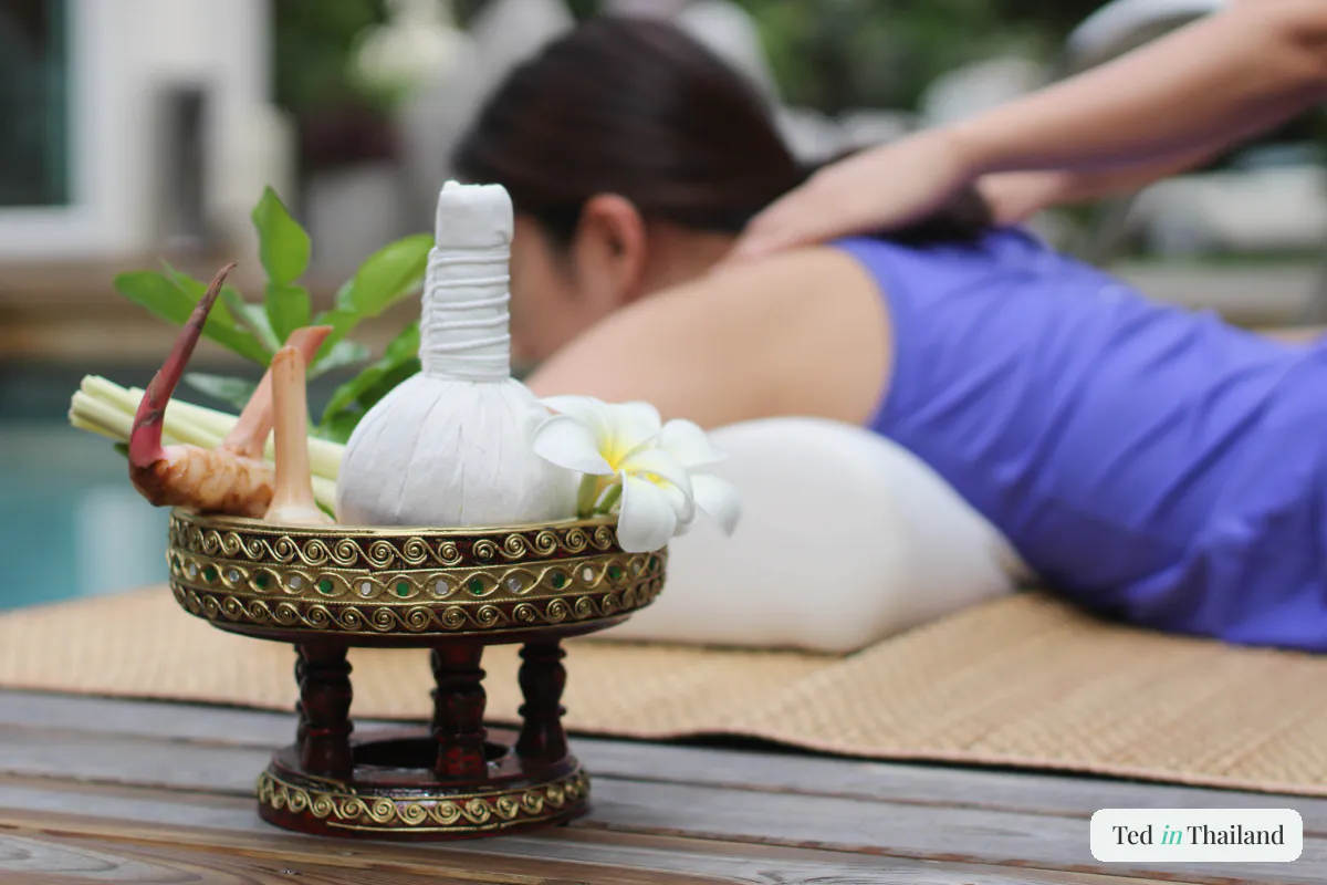 A Thai herbal compress ball with frangipani and lemongrass beside a poolside massage at a Koh Samui spa