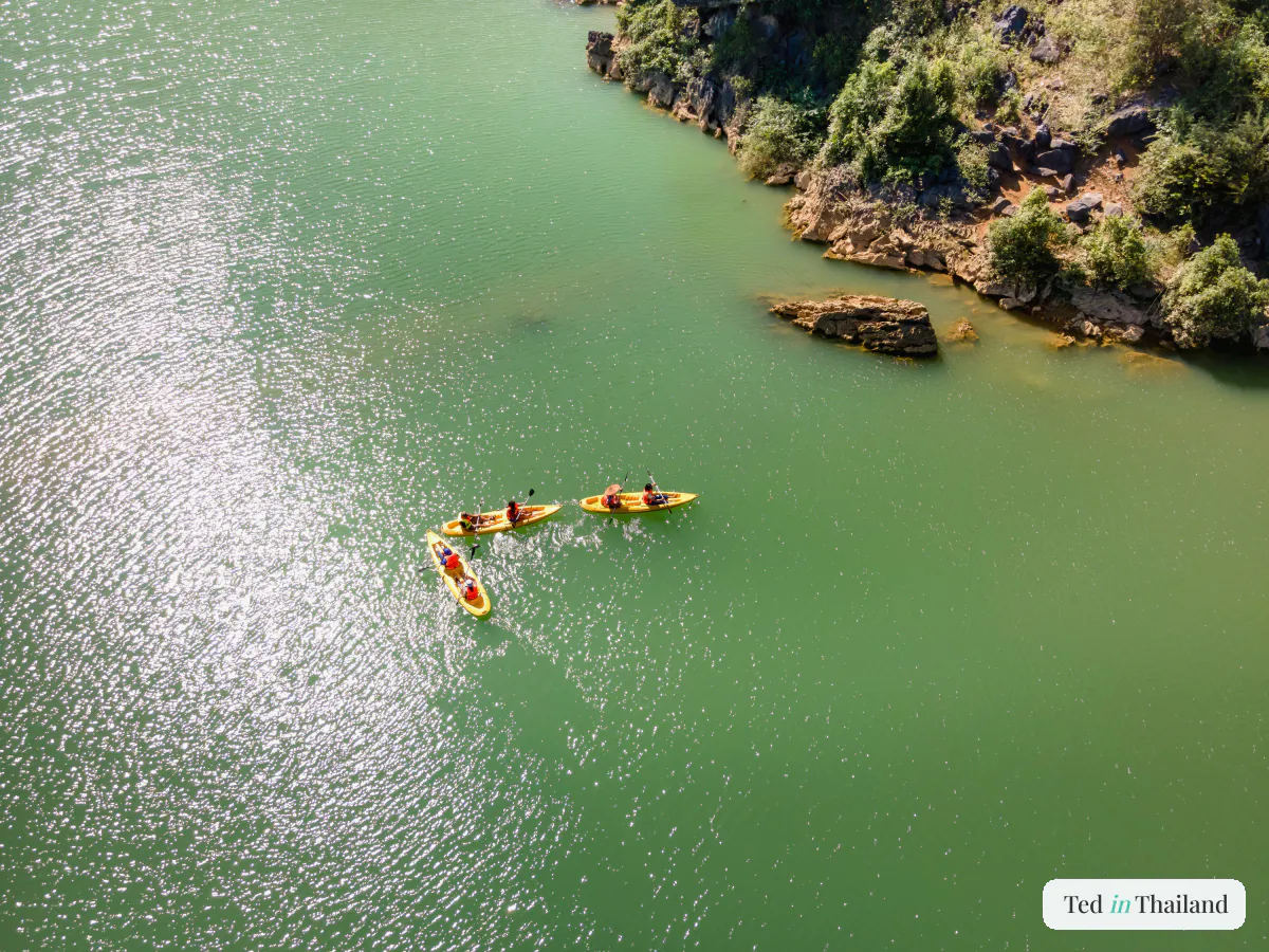 Kayakers paddling bright boats along calm green water beneath rocky cliffs at Ang Thong National Marine Park