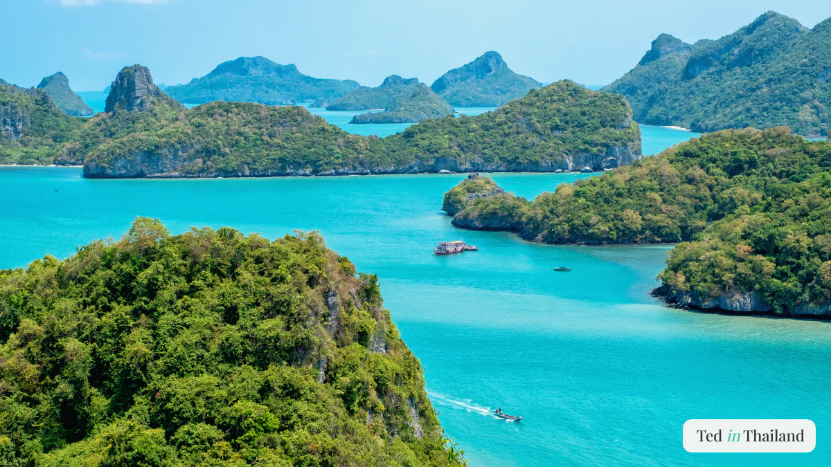 A red tour boat and a speedboat crossing a turquoise channel between limestone cliffs at Ang Thong marine park near Koh Samui
