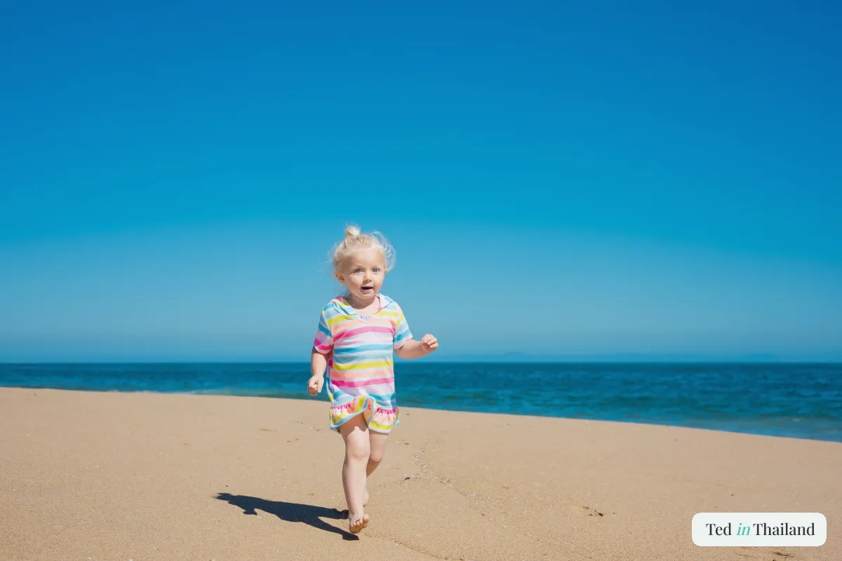 A toddler running barefoot across the sand at the water's edge on a shallow Koh Samui beach