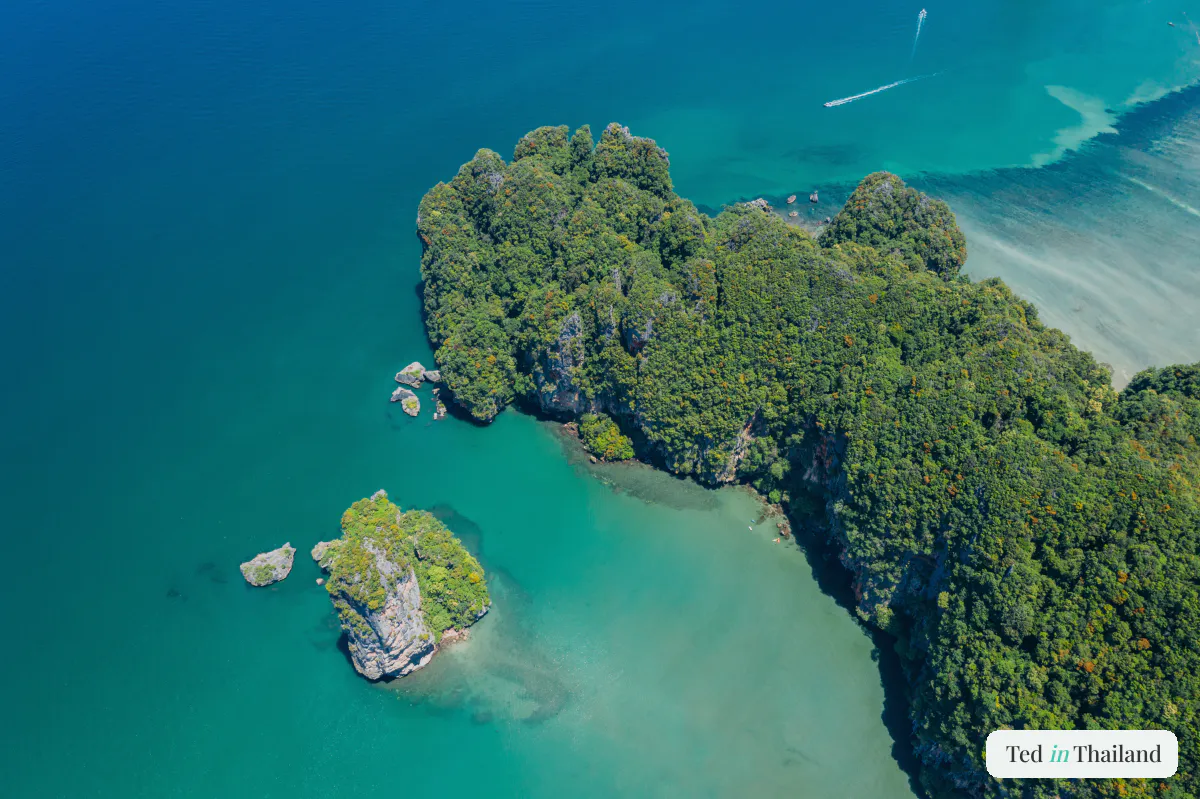 Aerial view of a jungle-covered headland and tiny islet ringed by vivid turquoise water off the coast of Koh Samui