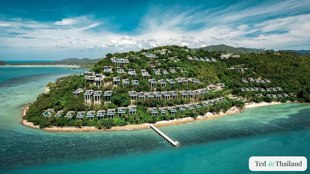Aerial view of Conrad Koh Samui's private headland, pool villas stepping down the forested slope to a jetty over the reef