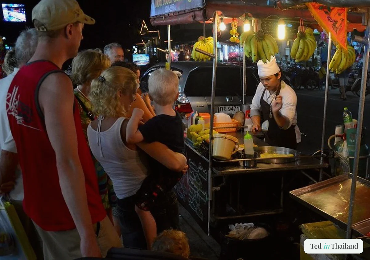 A vendor cooking banana roti pancakes on a griddle at a night-market food stall on Koh Samui