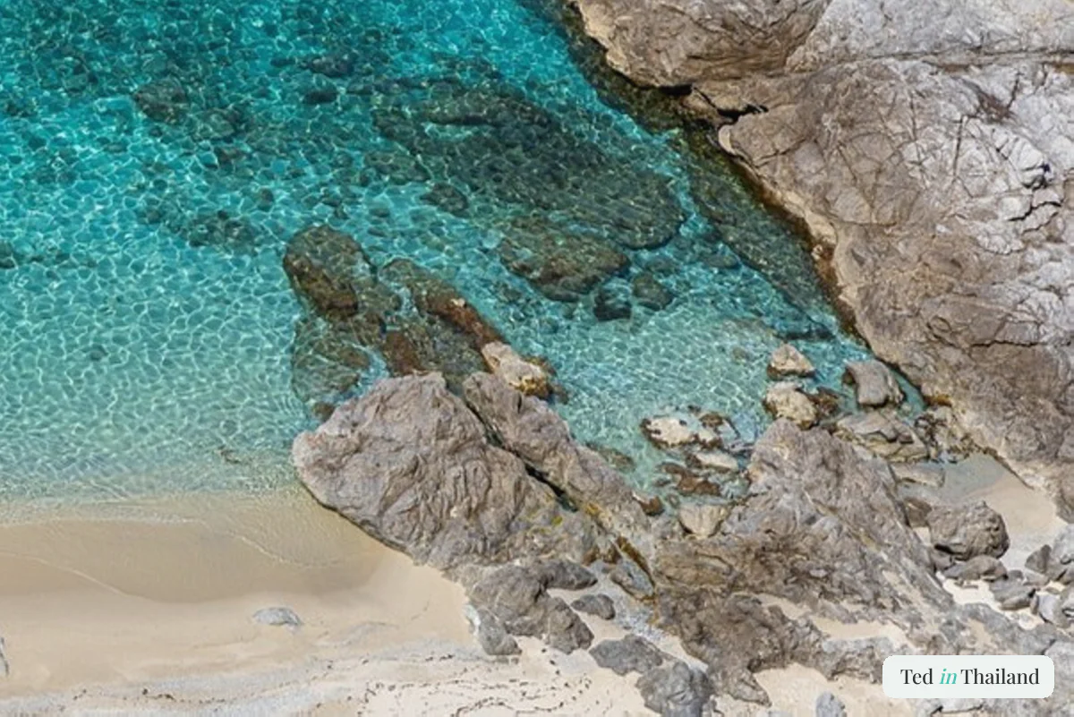 Clear shallow water over a rocky seabed in a quiet Koh Samui cove, similar to Taling Ngam Beach at low tide