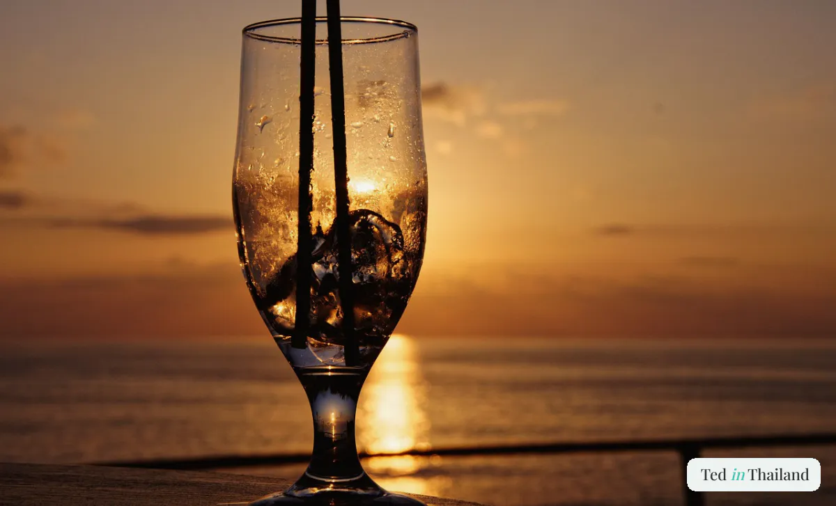 Iced drink silhouetted against an orange Koh Samui sunset over the sea at a beach bar