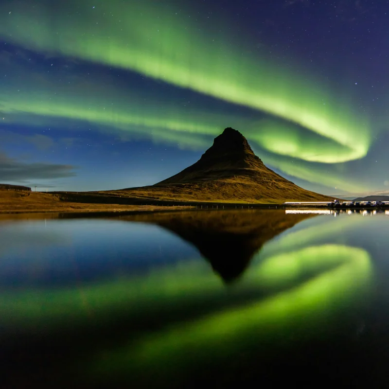 Aurora borealis in green above a mountain reflected in a calm lake at night.