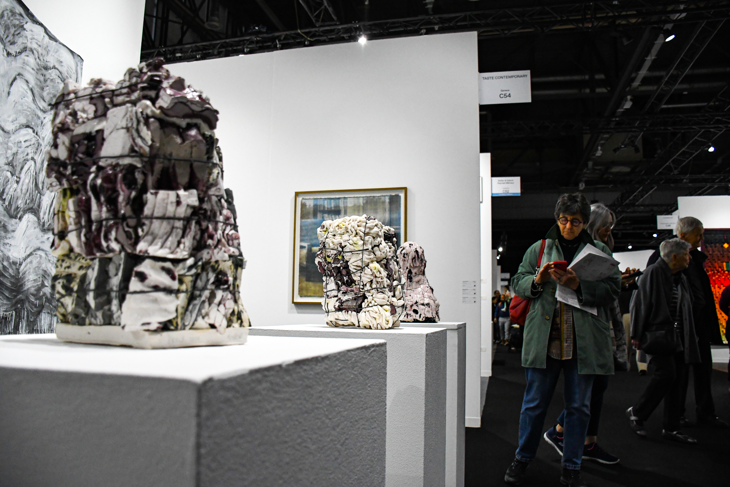 Art gallery exhibition with abstract sculptures on white pedestals and visitors viewing the displays.