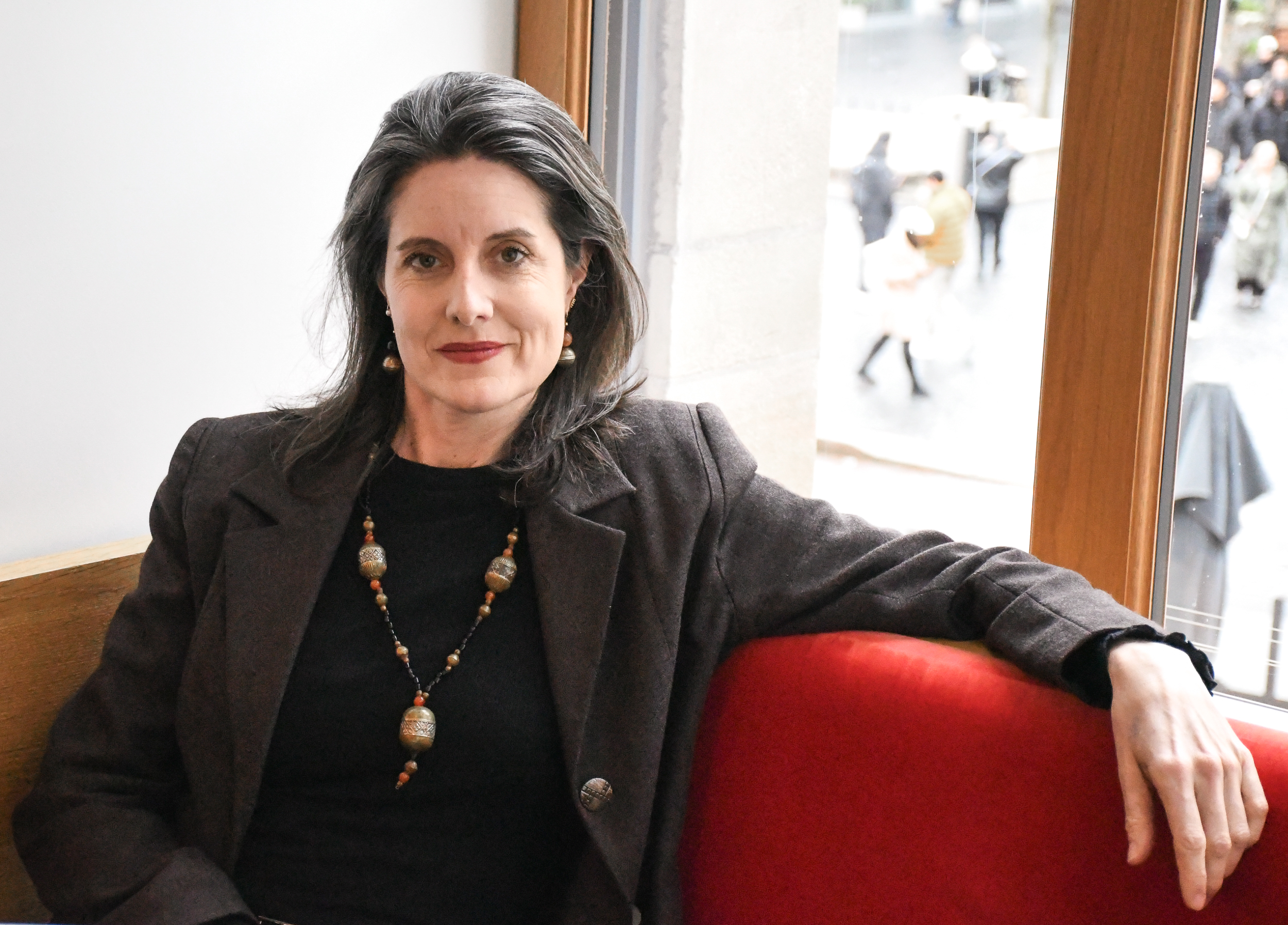 A woman poses for a professional portrait sitting on a red couch in a hotel lobby. 
