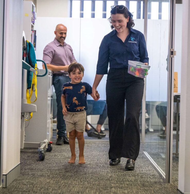 Woman holding a child's hand walking down an office hallway, both smiling.
