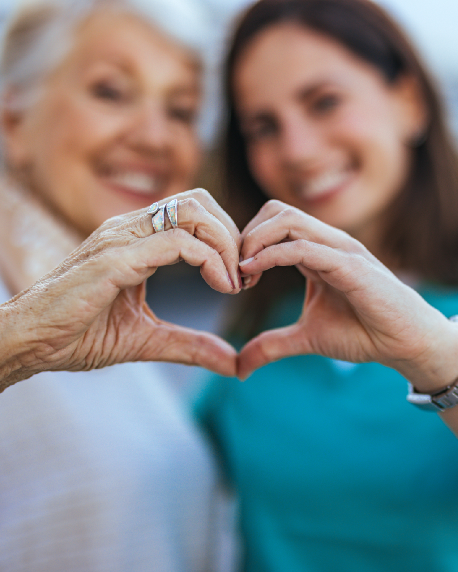 Elderly woman and younger woman forming a heart shape with their hands, smiling together.