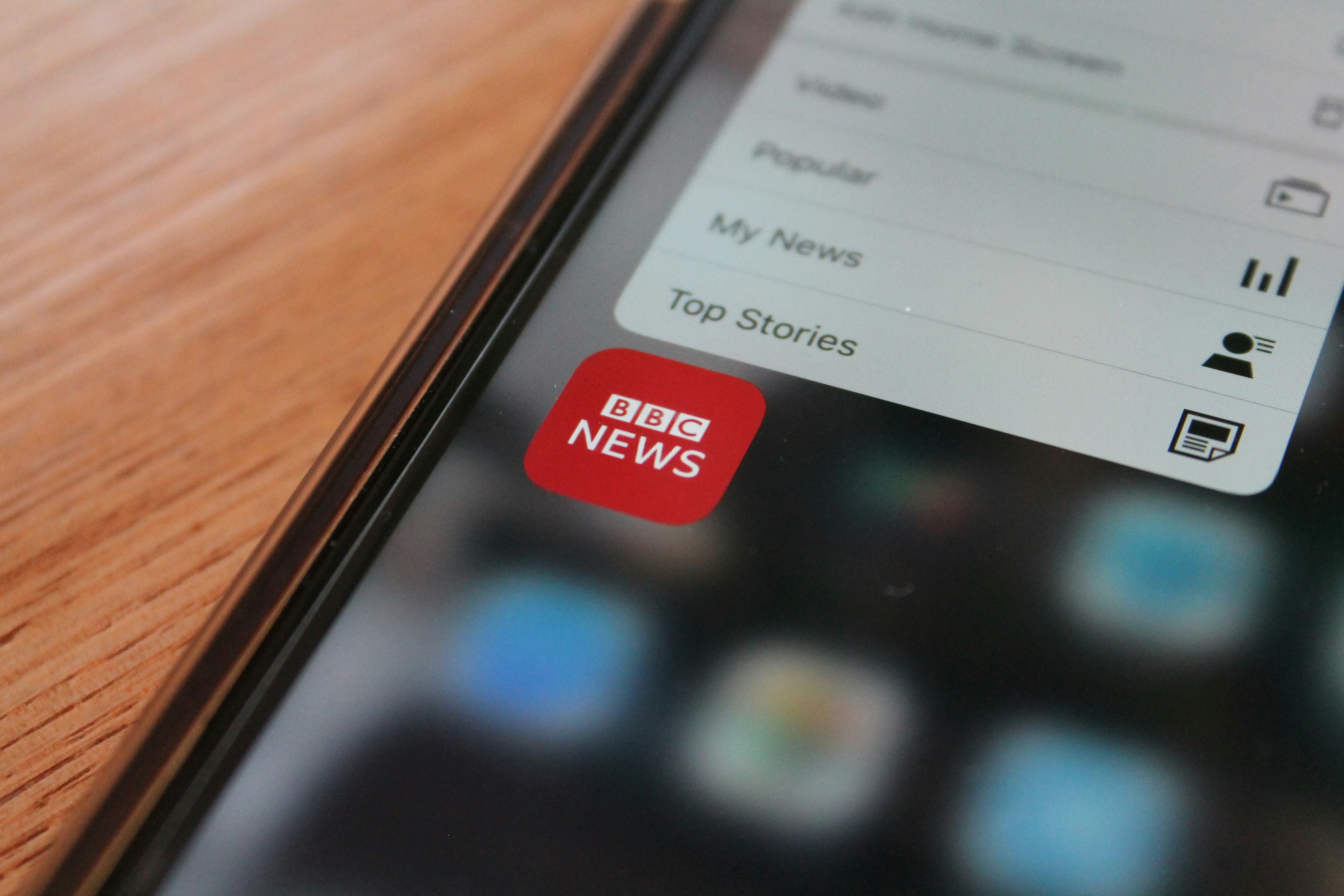 the image is a picture of a phone, the screen is showing the logo of the app "bbc news", written in white on a red background