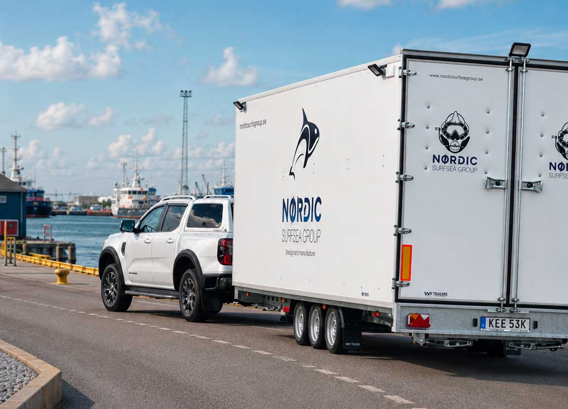 Vit pickup-bil med stor vit släpvagn kör längs kajen