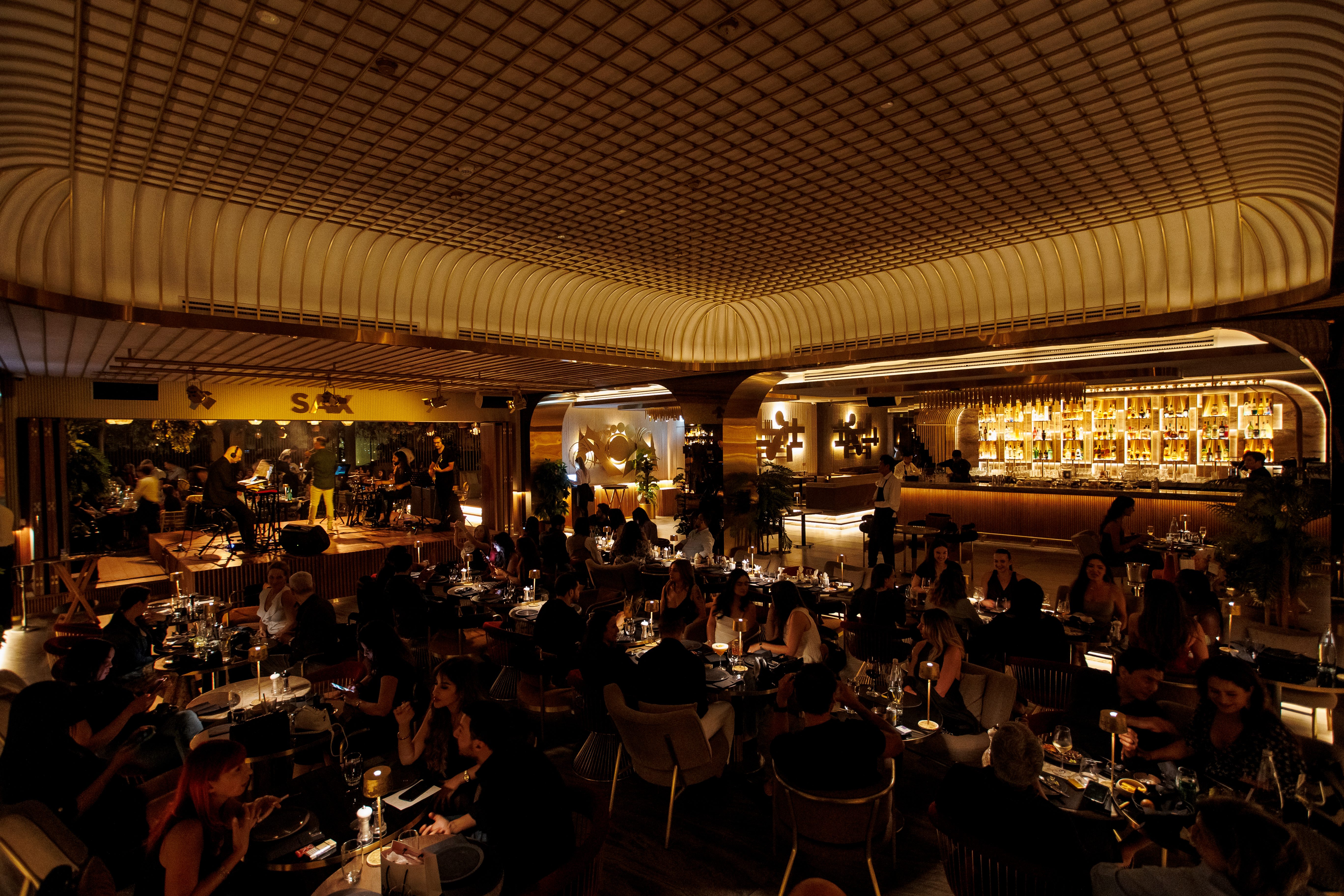 Dimly lit upscale restaurant with patrons dining and live band performing on stage.
