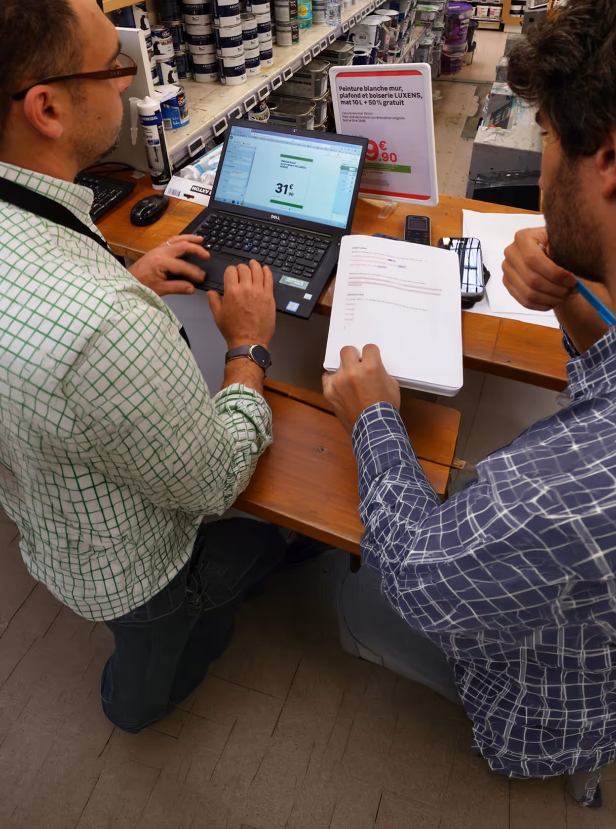 Deux hommes regardent un ordinateur portable et des documents dans un magasin de peinture.