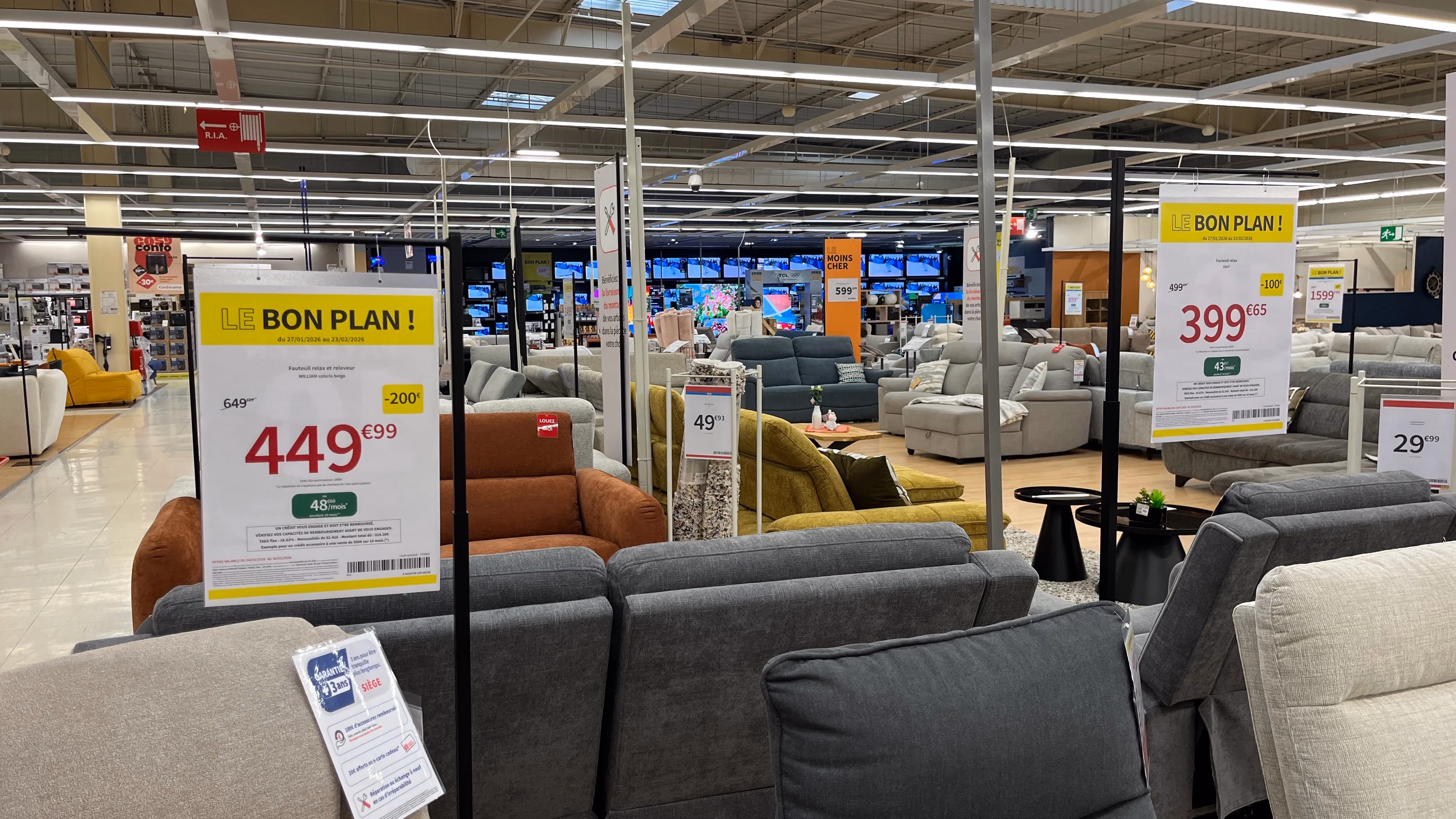 Affiches prix promotionnelles suspendues dans un rayon de canapés, avec prix barré, remise et mensualité de financement