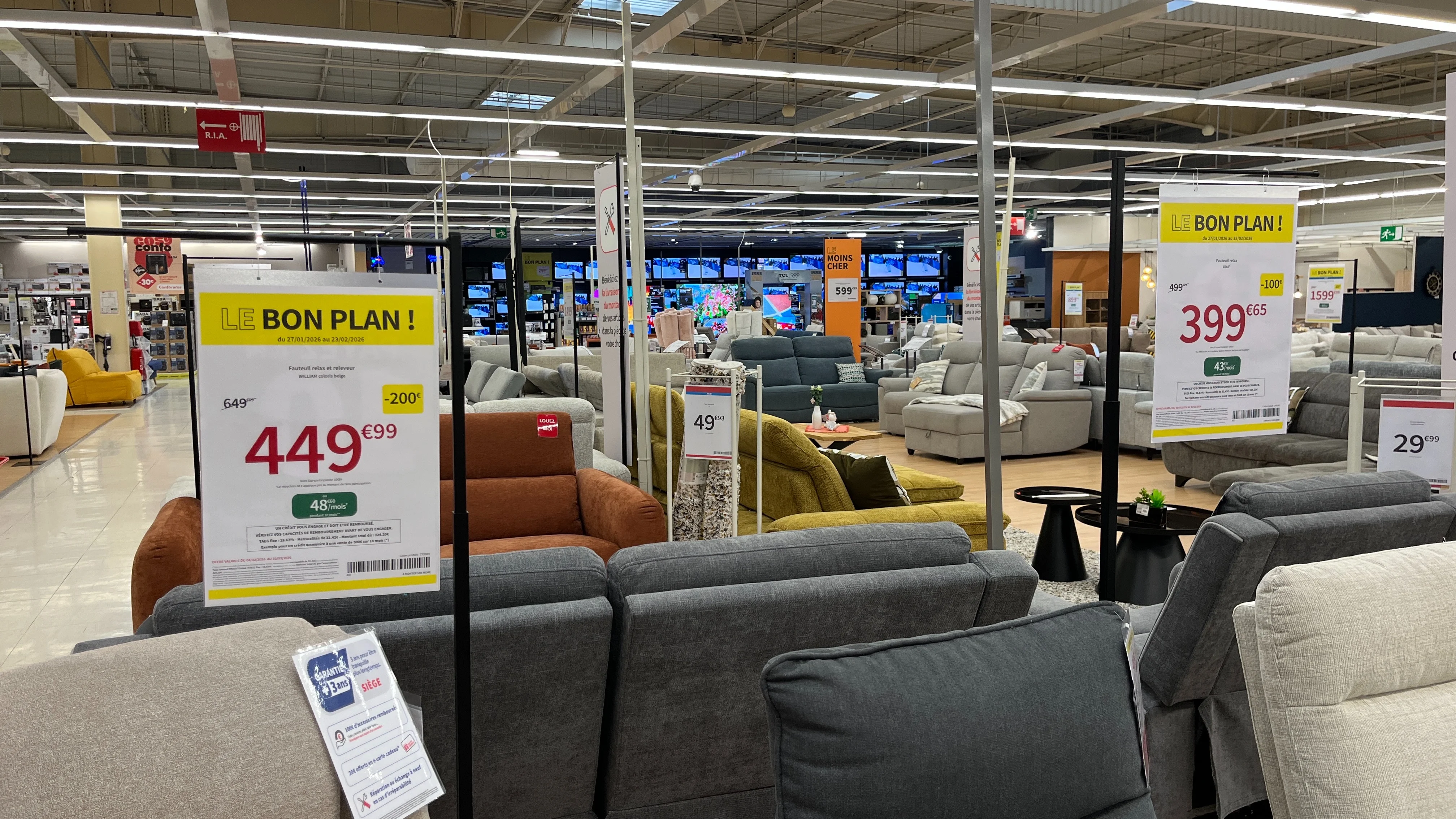 Affiches prix promotionnelles suspendues dans un rayon de canapés, avec prix barré, remise et mensualité de financement