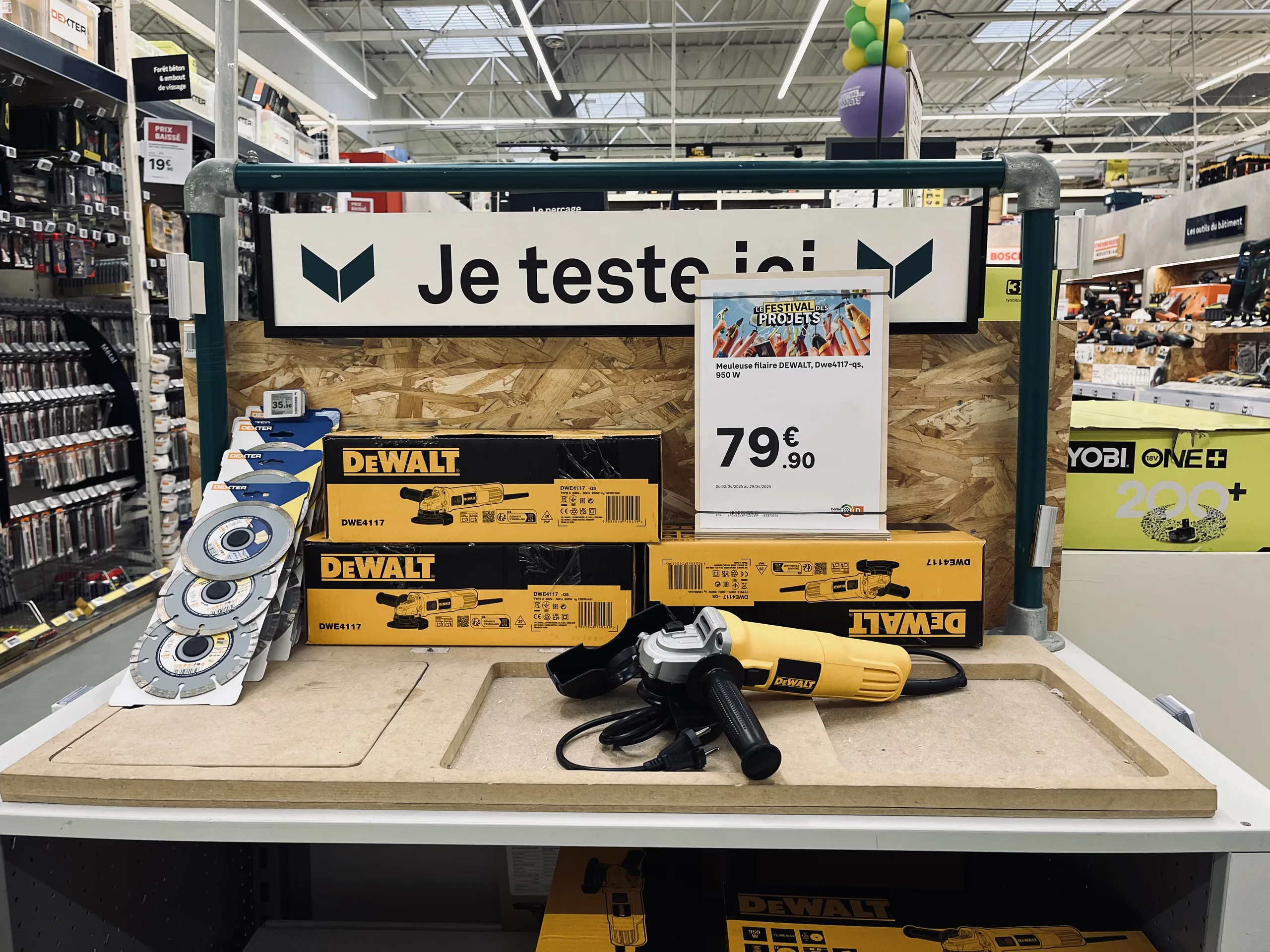 Espace de démonstration d'outillage avec un panneau « Je teste ici » et une affiche prix de meuleuse posée sur le plan de travail
