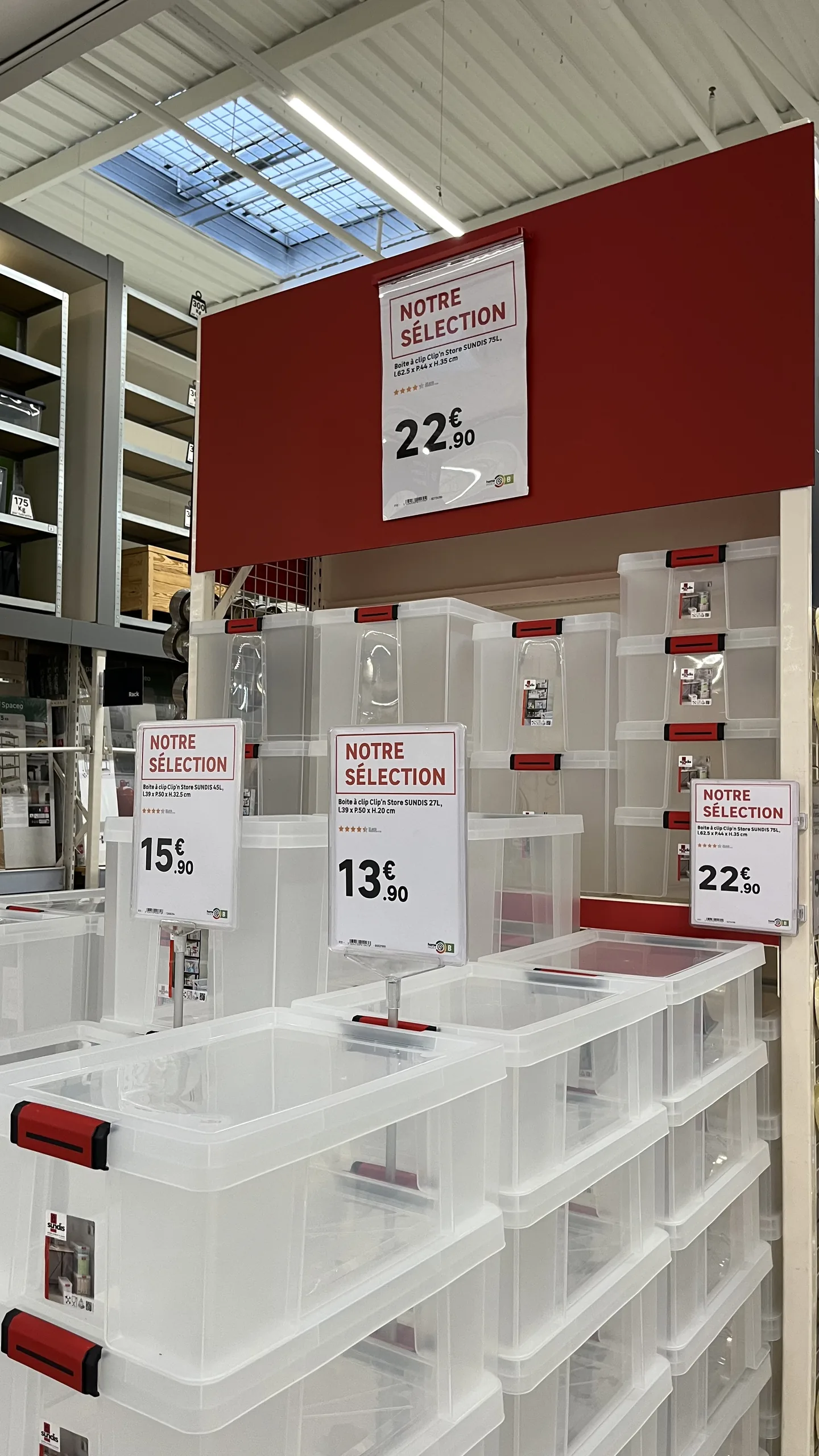 Rayon de boîtes de rangement avec plusieurs affiches « Notre sélection » de tailles différentes indiquant les prix