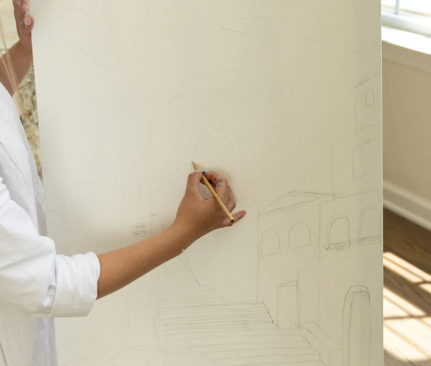 Person sketching architectural shapes with a pencil on a large canvas or paper.