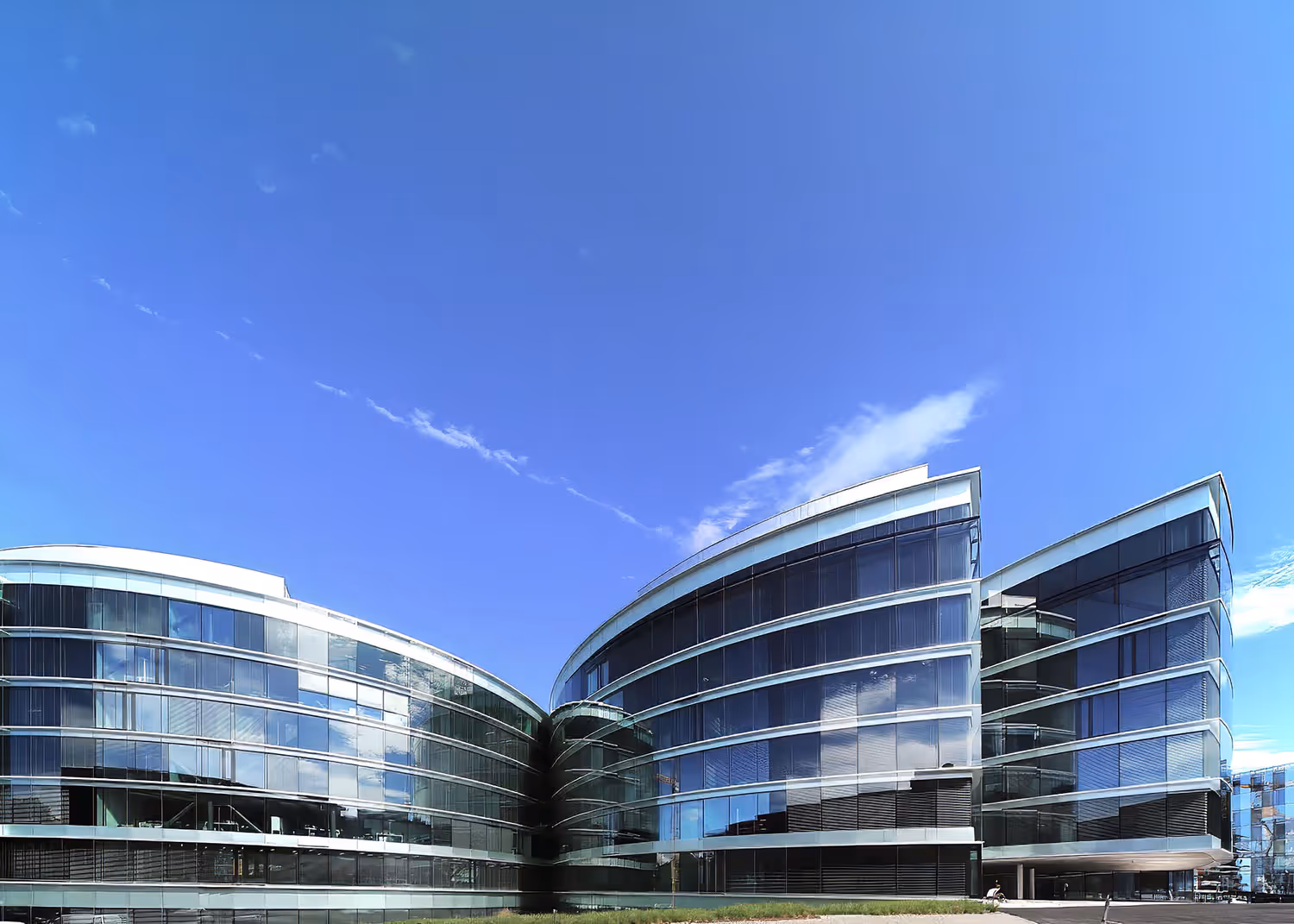 Modern curved glass office building under a clear blue sky.