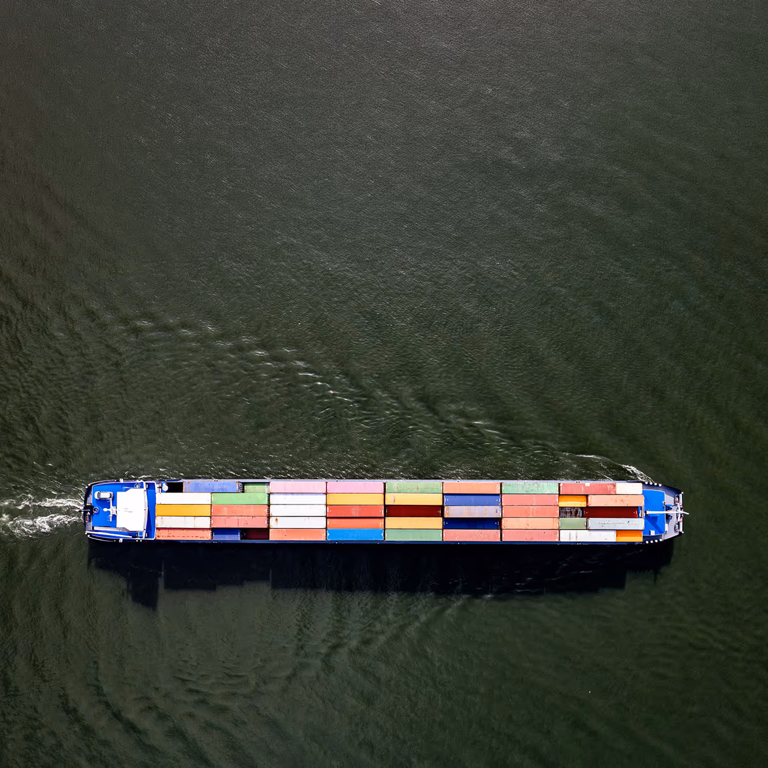 Aerial view of a cargo ship carrying multicolored shipping containers on green water.
