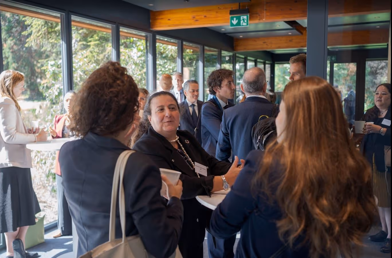 Professionals networking and conversing in a bright corridor with large windows during a business event.